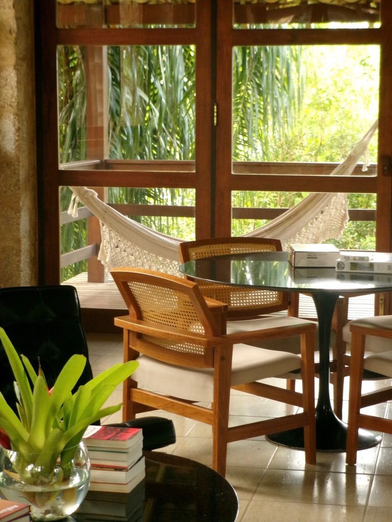Varanda aconchegante com cadeiras de vime, mesa de vidro e rede com vista para a vegetação exuberante.