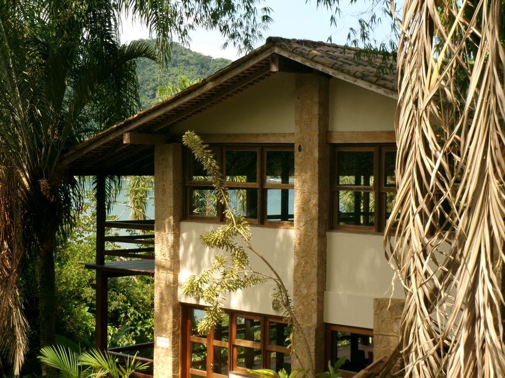 Casa tropical com varandas de madeira e telhado inclinado, rodeada por palmeiras exuberantes.