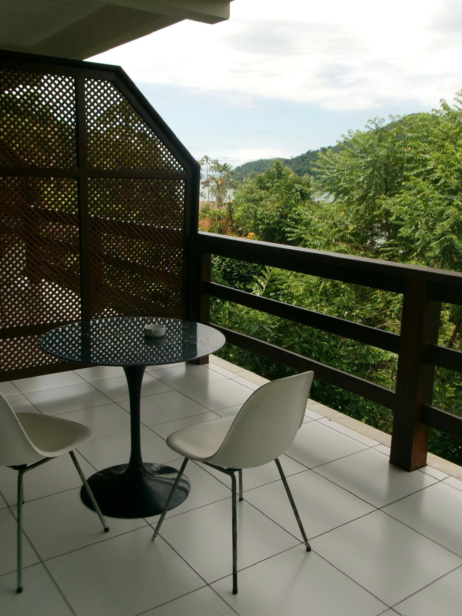Varanda com mesa redonda e cadeiras, com vista para colinas verdes e árvores.
