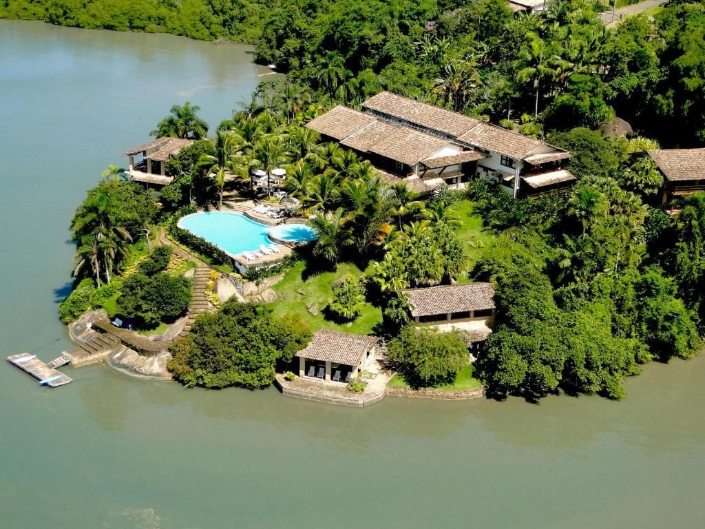 Um resort tropical em uma ilha exuberante com piscina turquesa, construções com telhados de palha e águas calmas.
