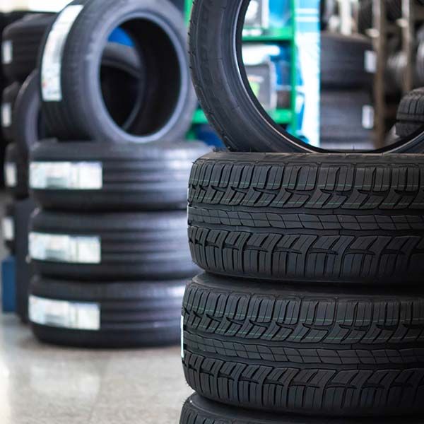 Stacks of black car tires in a shop, with one tire standing upright in the foreground.
