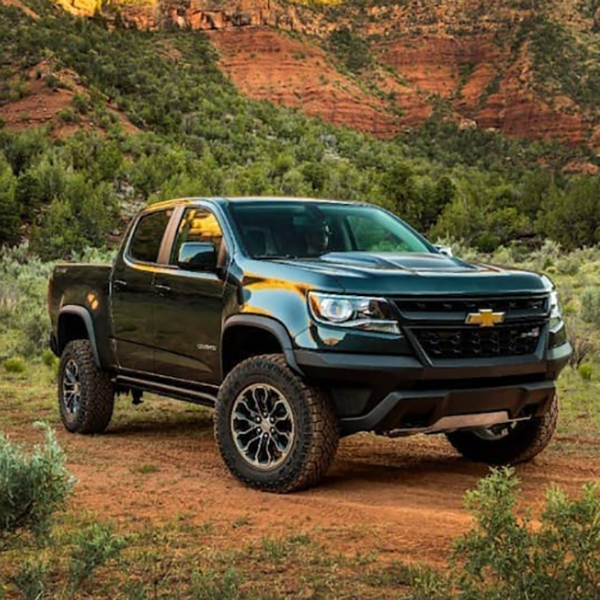 Black Chevrolet pickup truck on a red dirt trail with green shrubs and canyon cliffs in the background