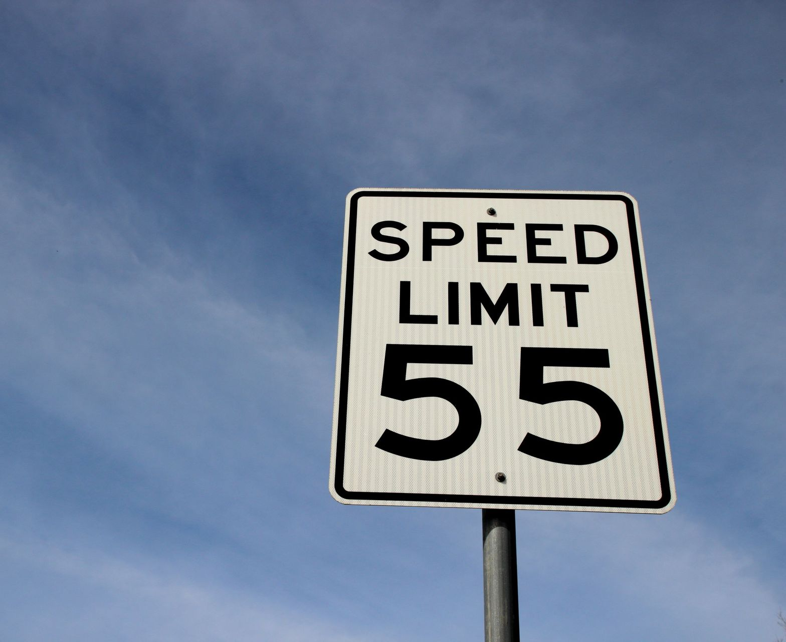 A rectangular white road sign against a blue sky, displaying 