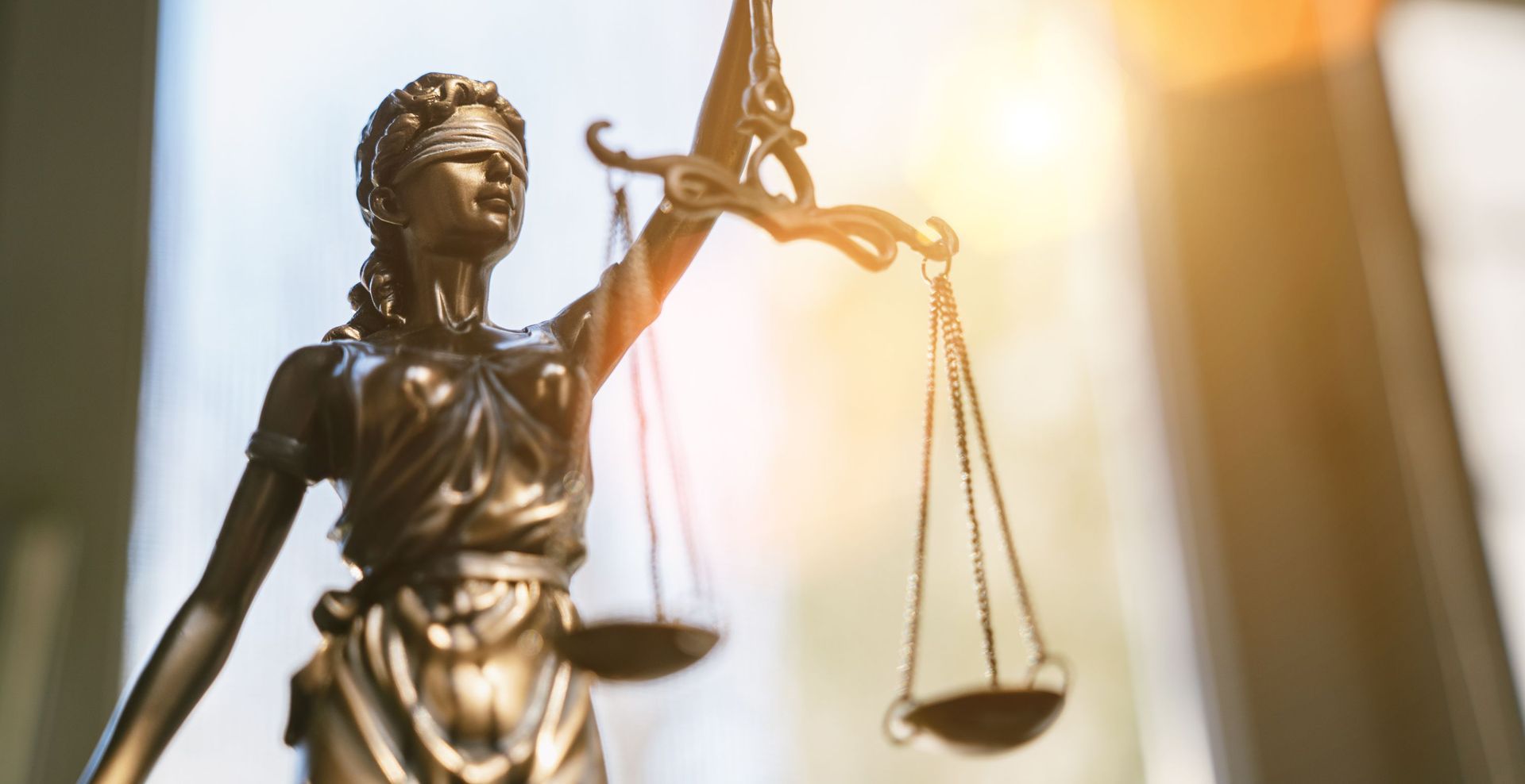 Bronze statue of Lady Justice holding scales, illuminated by warm light against a blurred background.