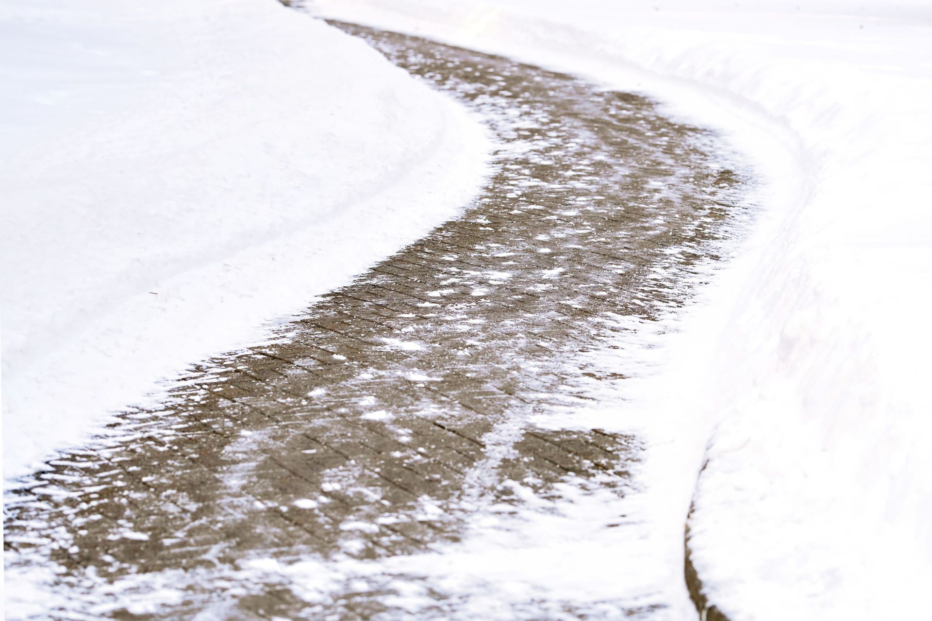 A curving concrete path partially cleared of snow, surrounded by thick, untouched snowbanks.