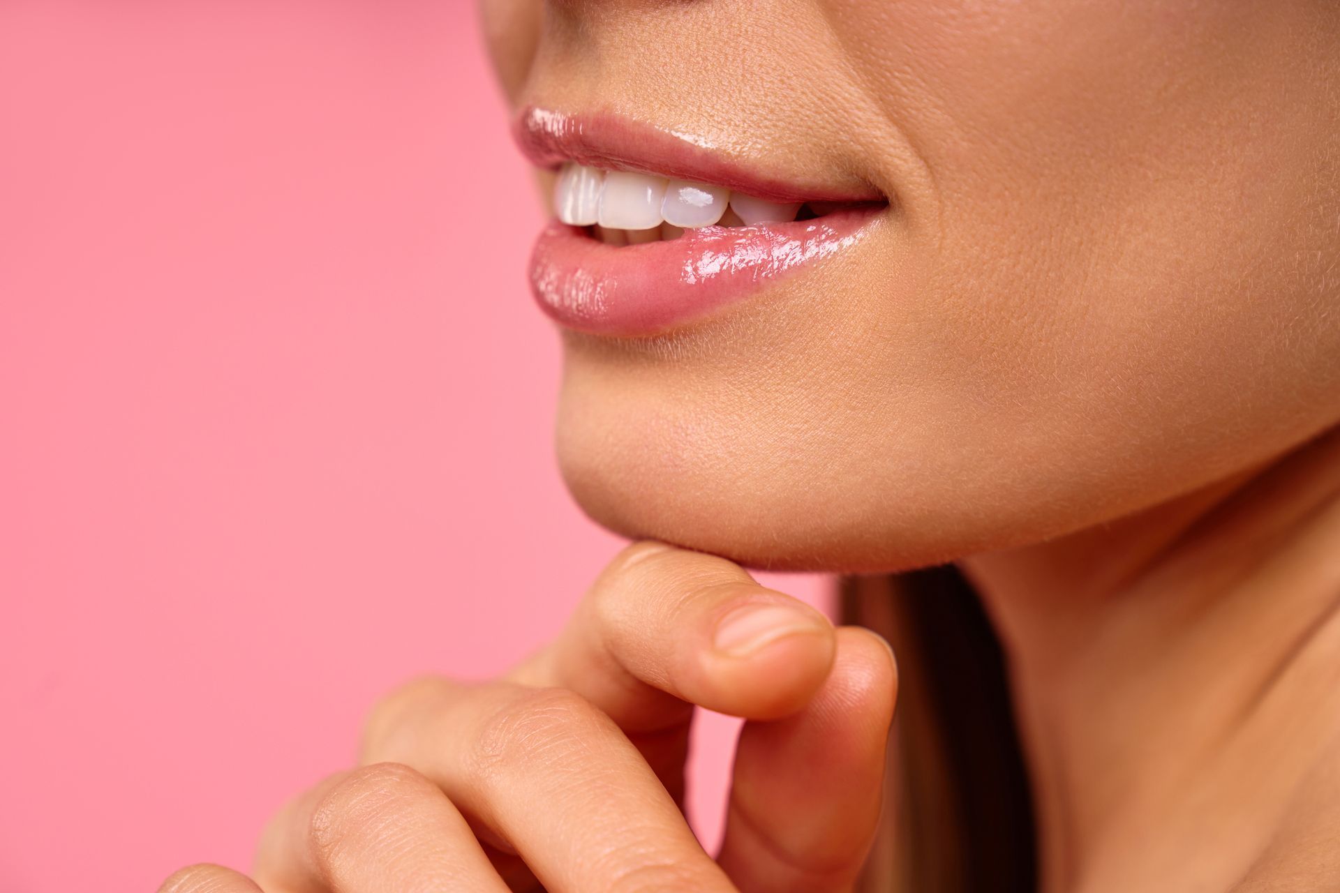 Close-up of a smiling mouth and chin with a hand touching the face against a pink background