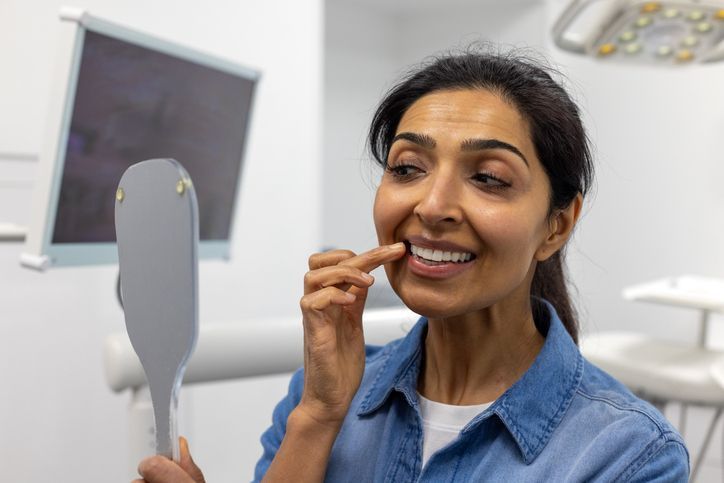 Woman using a handheld mirror to check her teeth in a bright bathroom