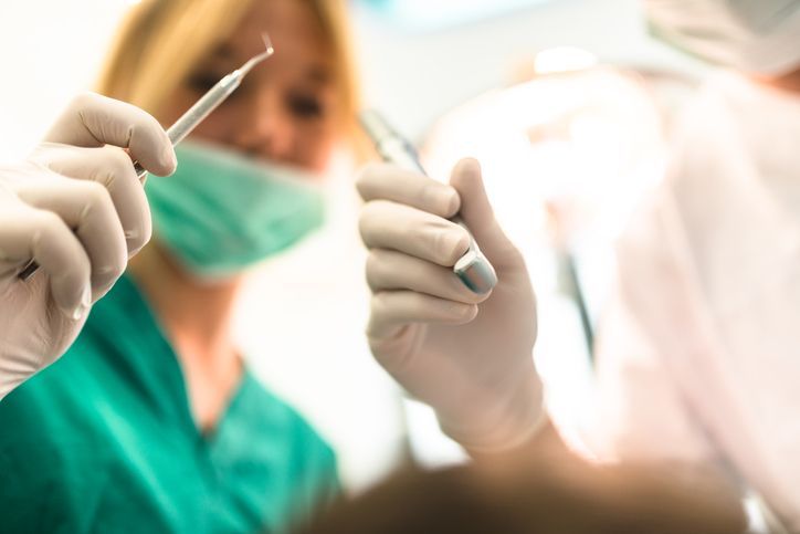 Gloved surgeon holding a scalpel in an operating room, with a masked colleague blurred in the background