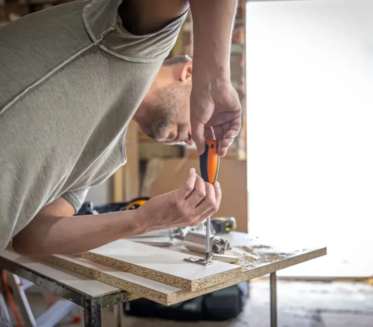 Person using a screwdriver to assemble a wooden board in a home renovation setting