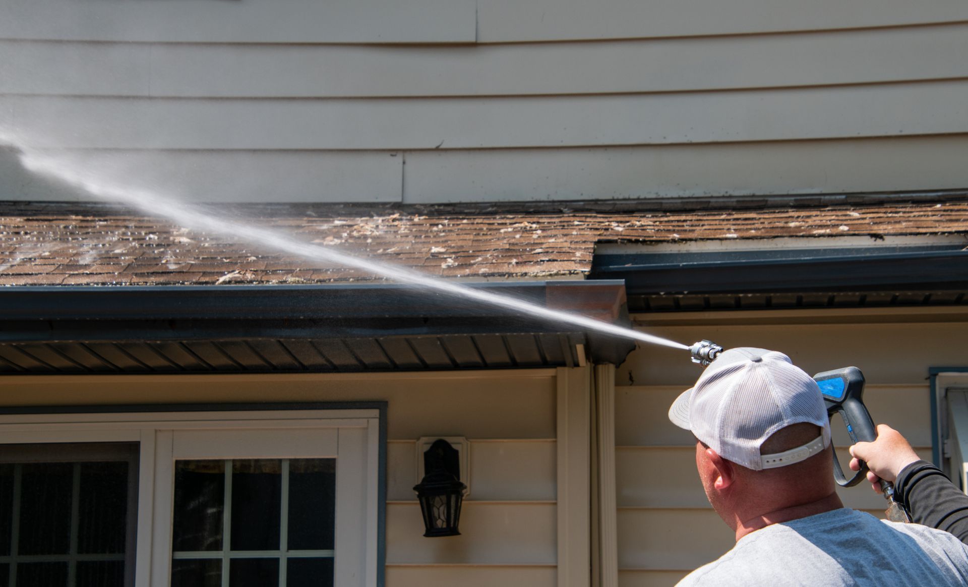 Man washing house siding with a pressure washer, spraying water along the roof edge