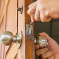 Hands pick a door lock with a key while another hand turns the silver knob