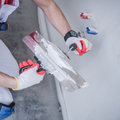 Person in red shirt smoothing white plaster on a wall with a trowel