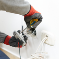 Electrician’s gloved hands working on exposed white wall wiring with tools.