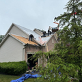 Workers roofing a white house with a ladder, under blue sky and surrounded by construction debris.