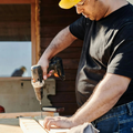 Man using a drill to work on a wooden board outside a cabin