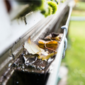 Leaves and debris clogging a rain gutter beside a house, with water pooling near the edge.