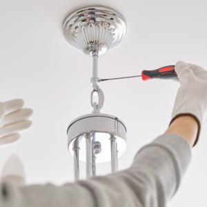 Gloved hands using a screwdriver to install a ceiling light fixture