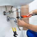 Person tightening bathroom sink pipes with a wrench under a white basin.