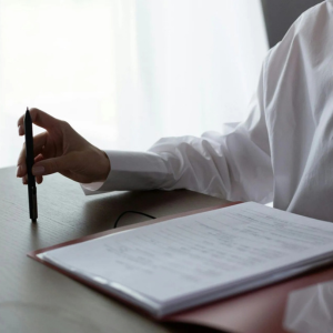 Hand holding a pen over an open notebook on a table by a bright window