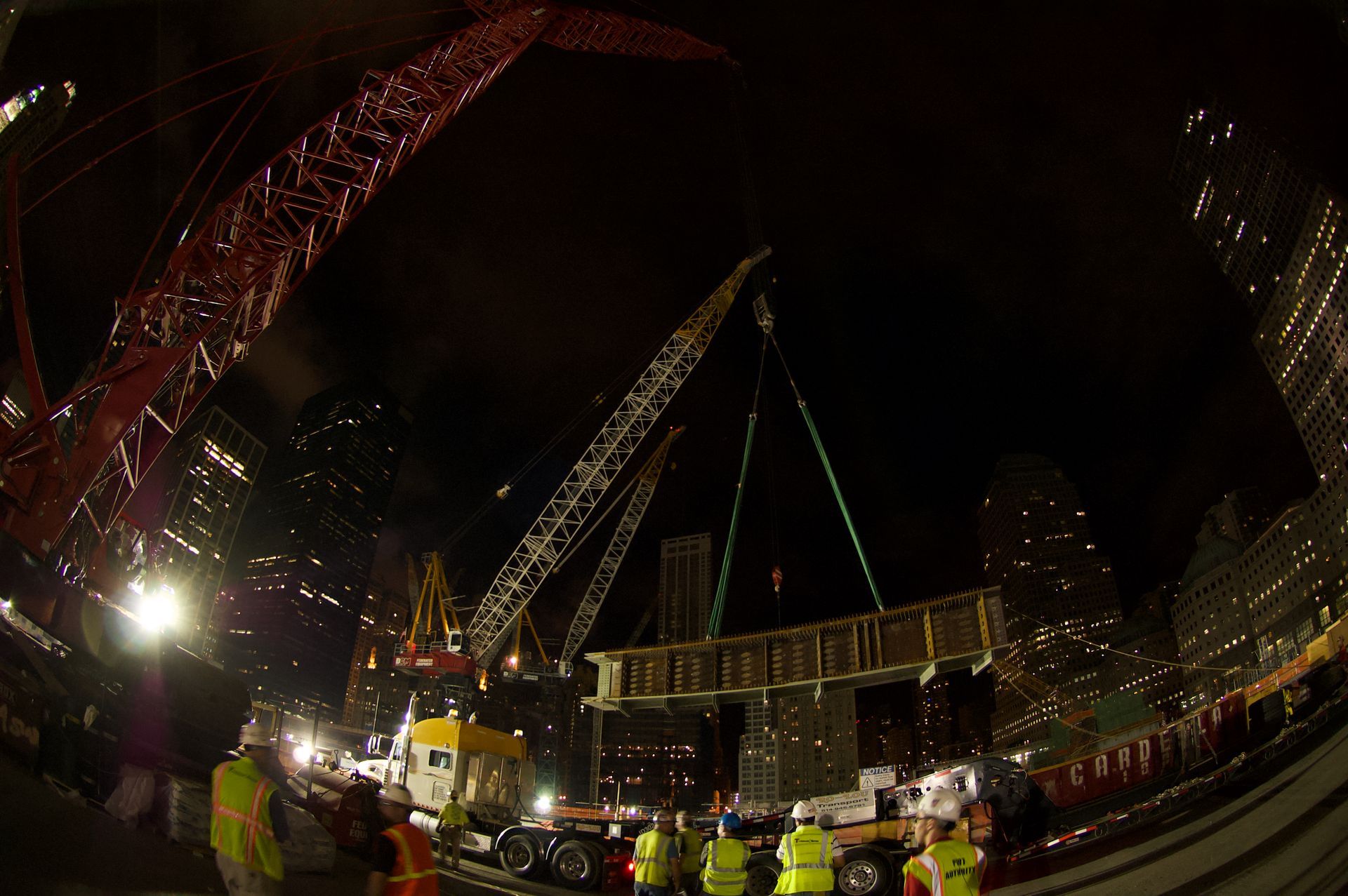 Night crane lift of a large structural steel assembly amid New York office towers.