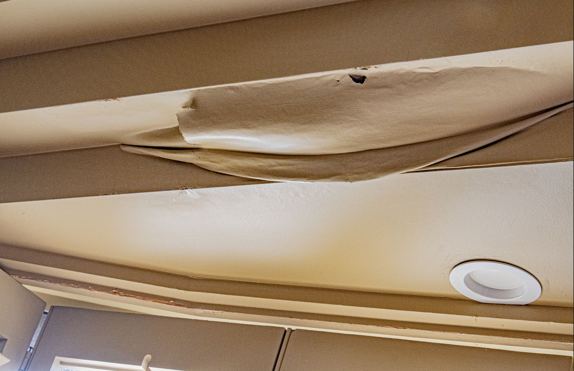 Buckled and detached ceiling finish beneath the lanai shows damage within the occupied space below.