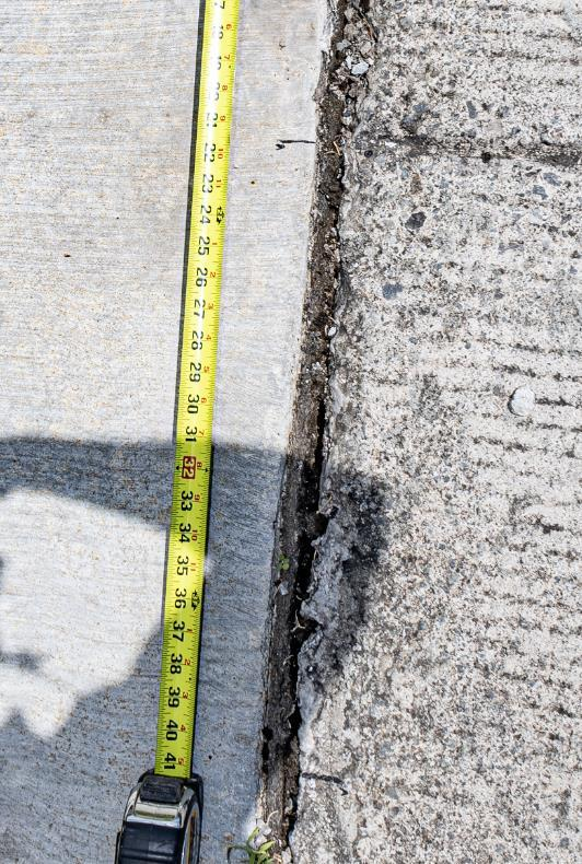 Tape measure beside displaced concrete at a driveway and garage-apron joint.