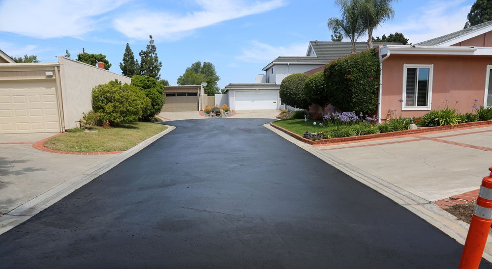 A residential street with a newly paved driveway between two houses.