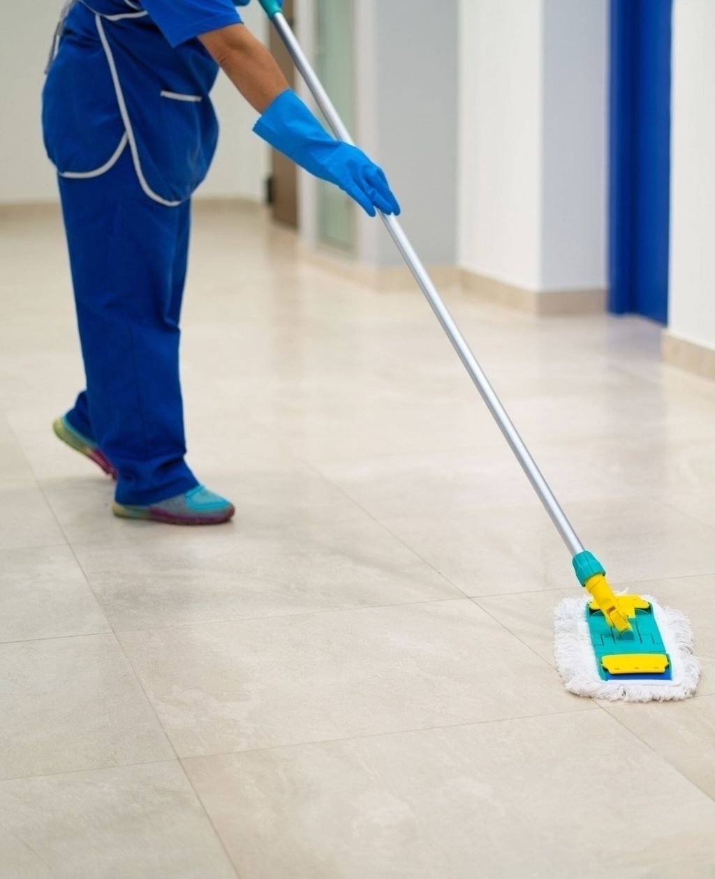 Una persona che indossa un camice blu lava il pavimento chiaro in un corridoio.