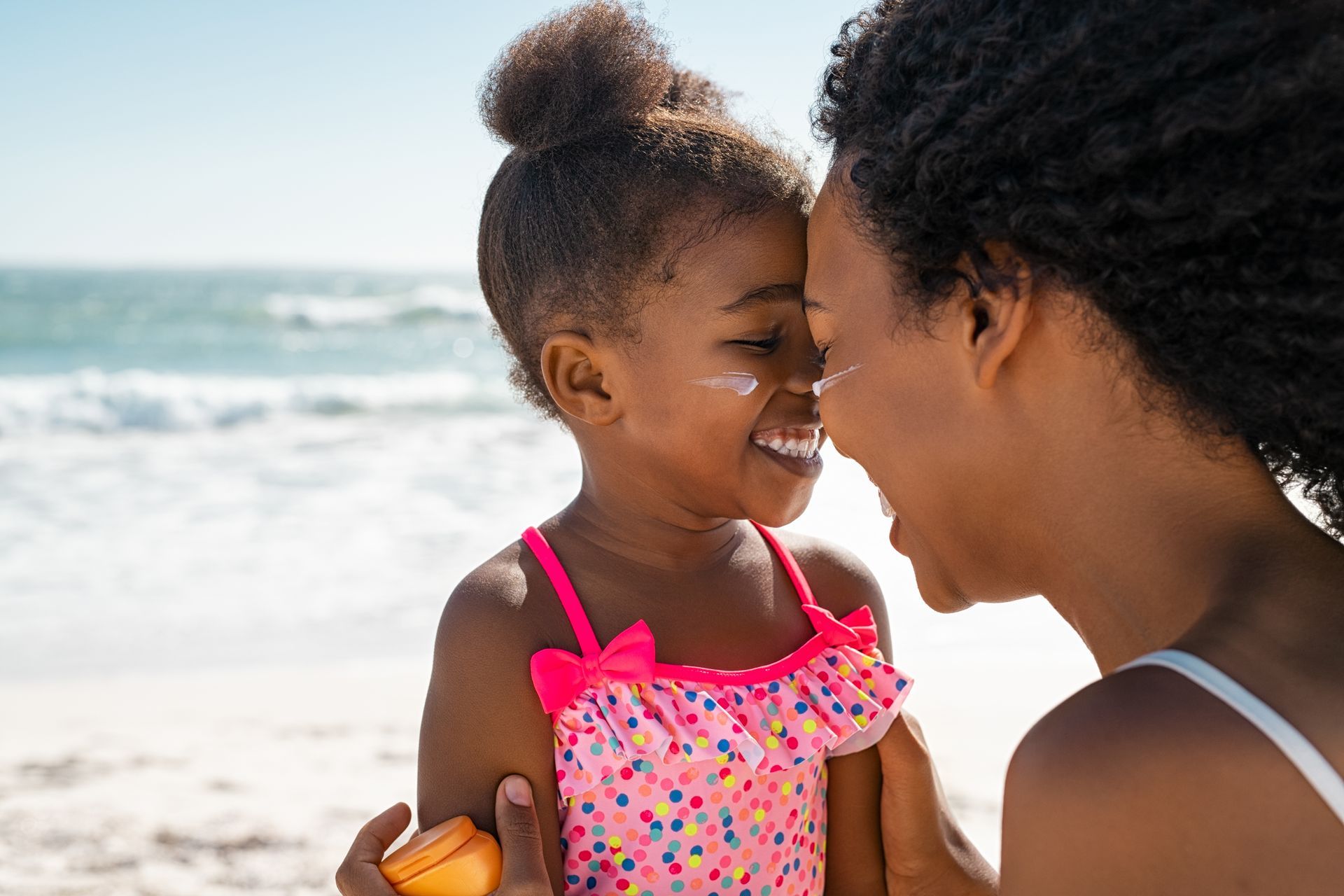A woman is applying sunscreen to her daughter 's face on the beach.