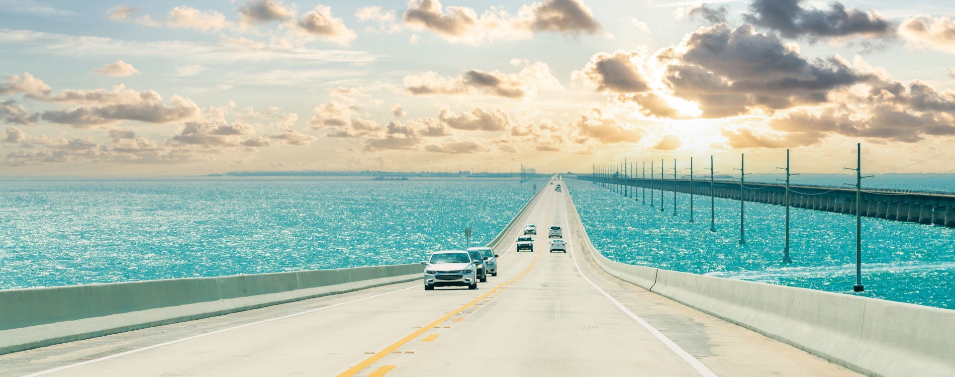Cars are driving on a bridge over the ocean at sunset.