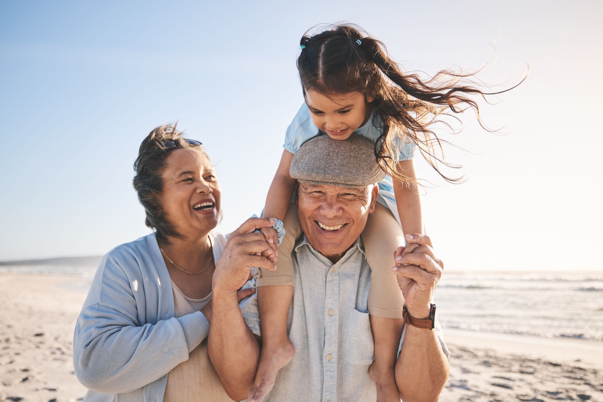 A grandma, grandpa and granddaughter are walking on the beach.
