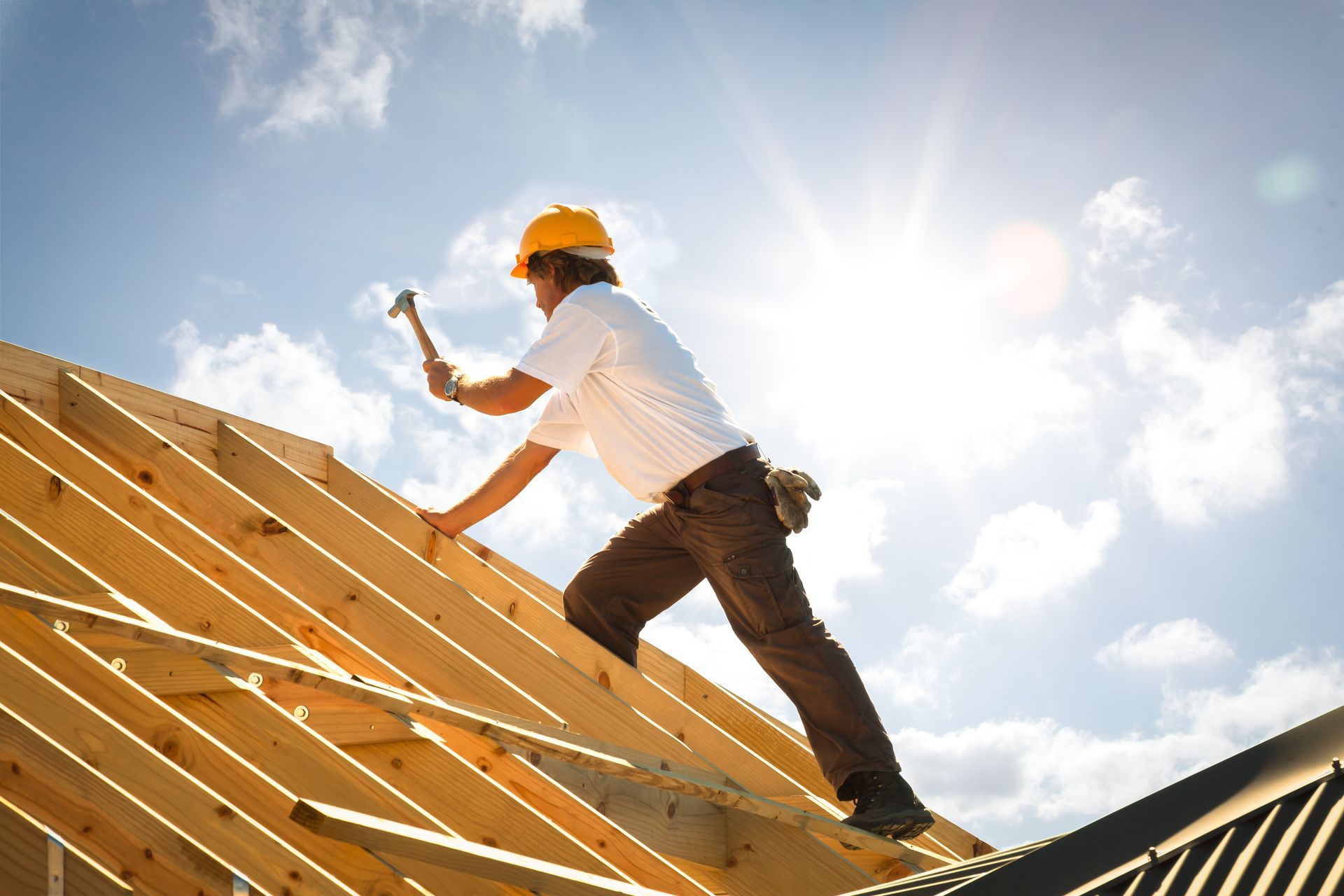 Roofing contractor installing wooden roof frame under bright sunlight during construction. Roofing contractor installing wooden roof frame under bright sunlight during construction.