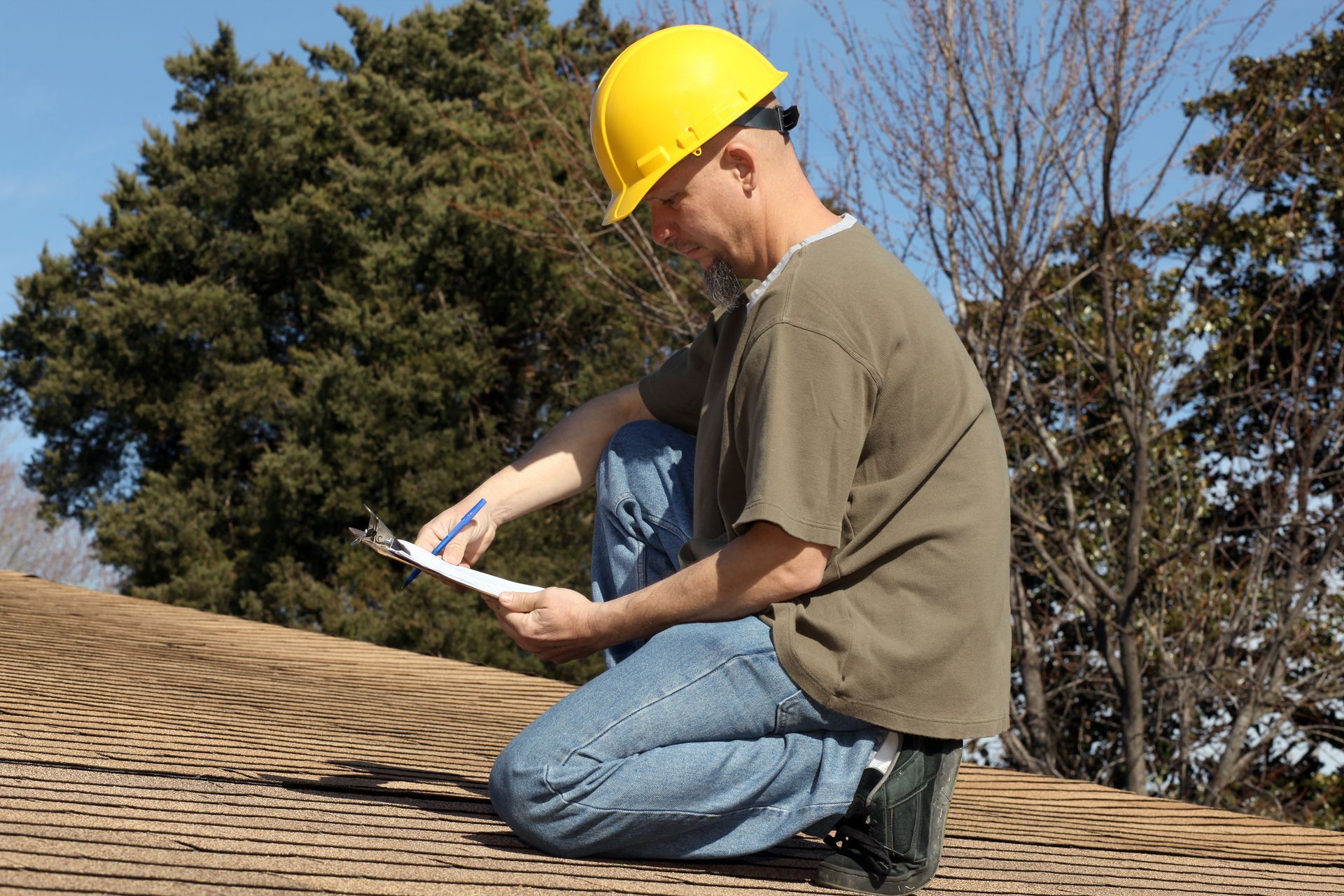 A man wearing a hard hat inspects a roof, performing a thorough home roofing inspection. A man wearing a hard hat inspects a roof, performing a thorough home roofing inspection.
