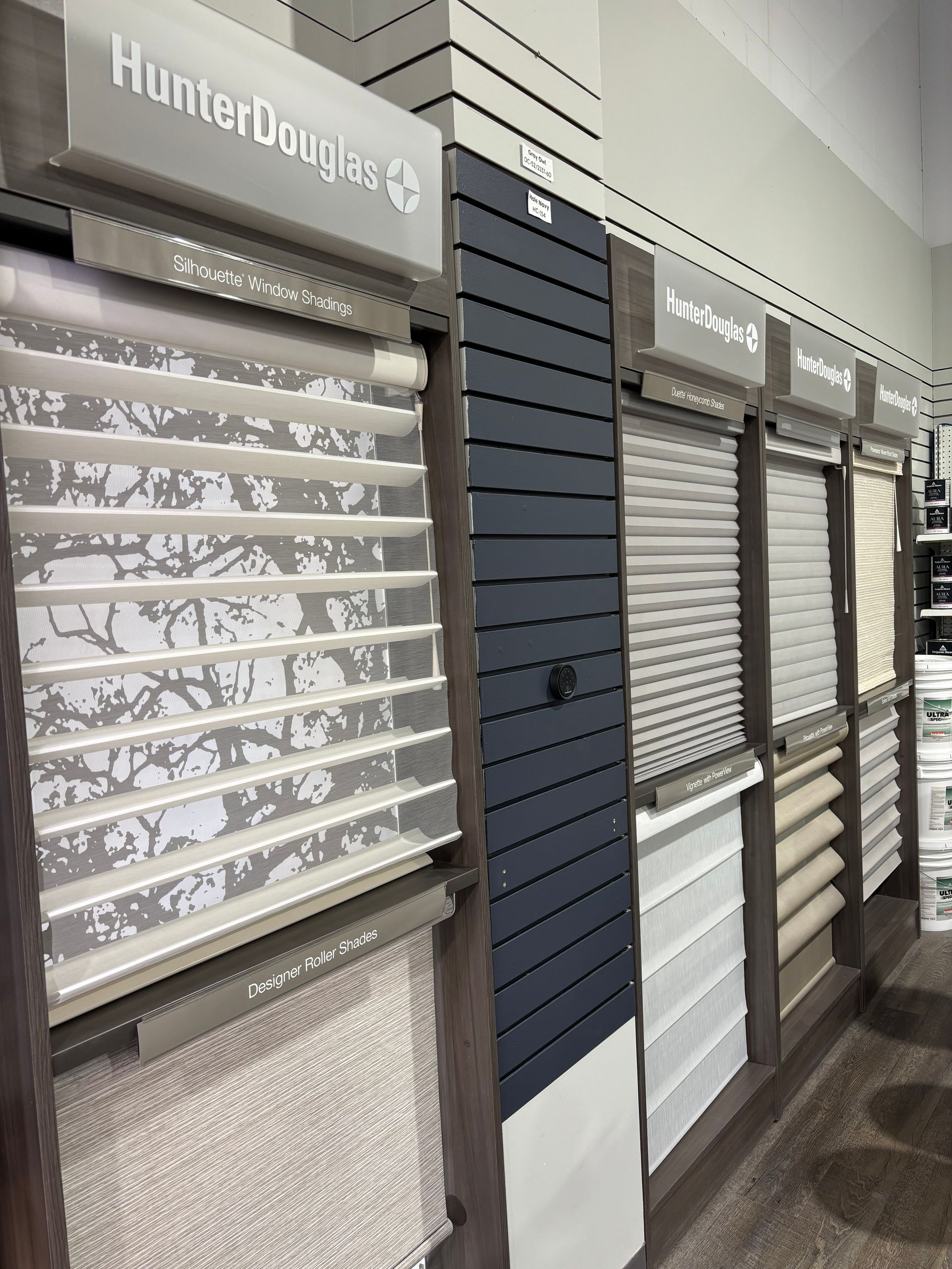 Rows of Hunter Douglas window blinds on display in a showroom, in gray and white tones.