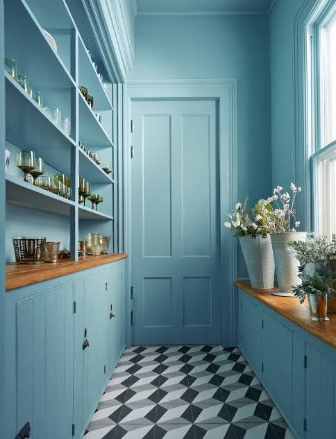 Light blue pantry with wooden countertops, white shelving, and black-and-white tiled floor.