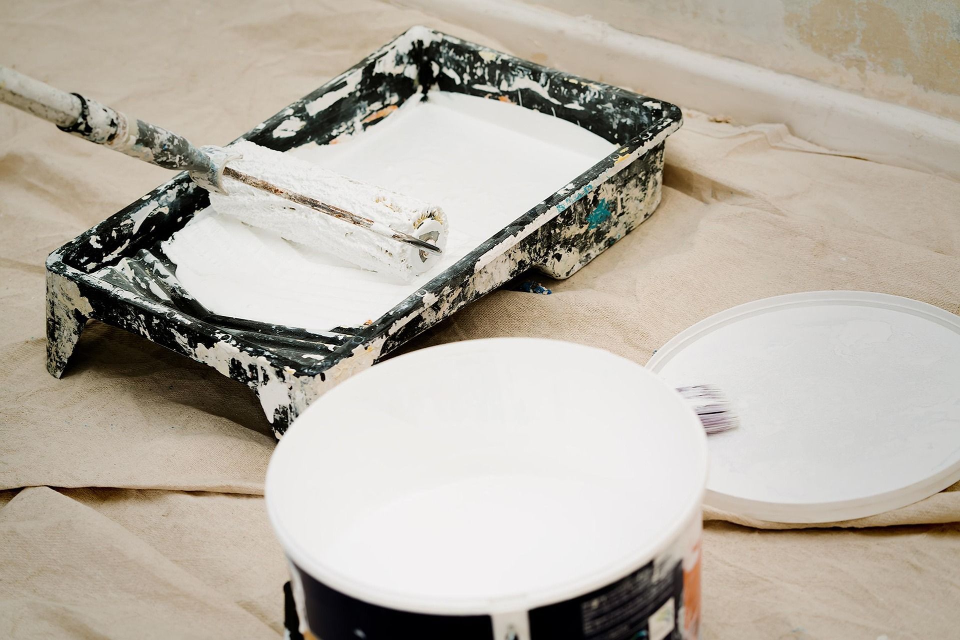 Paint roller in a tray filled with white paint; open paint can.