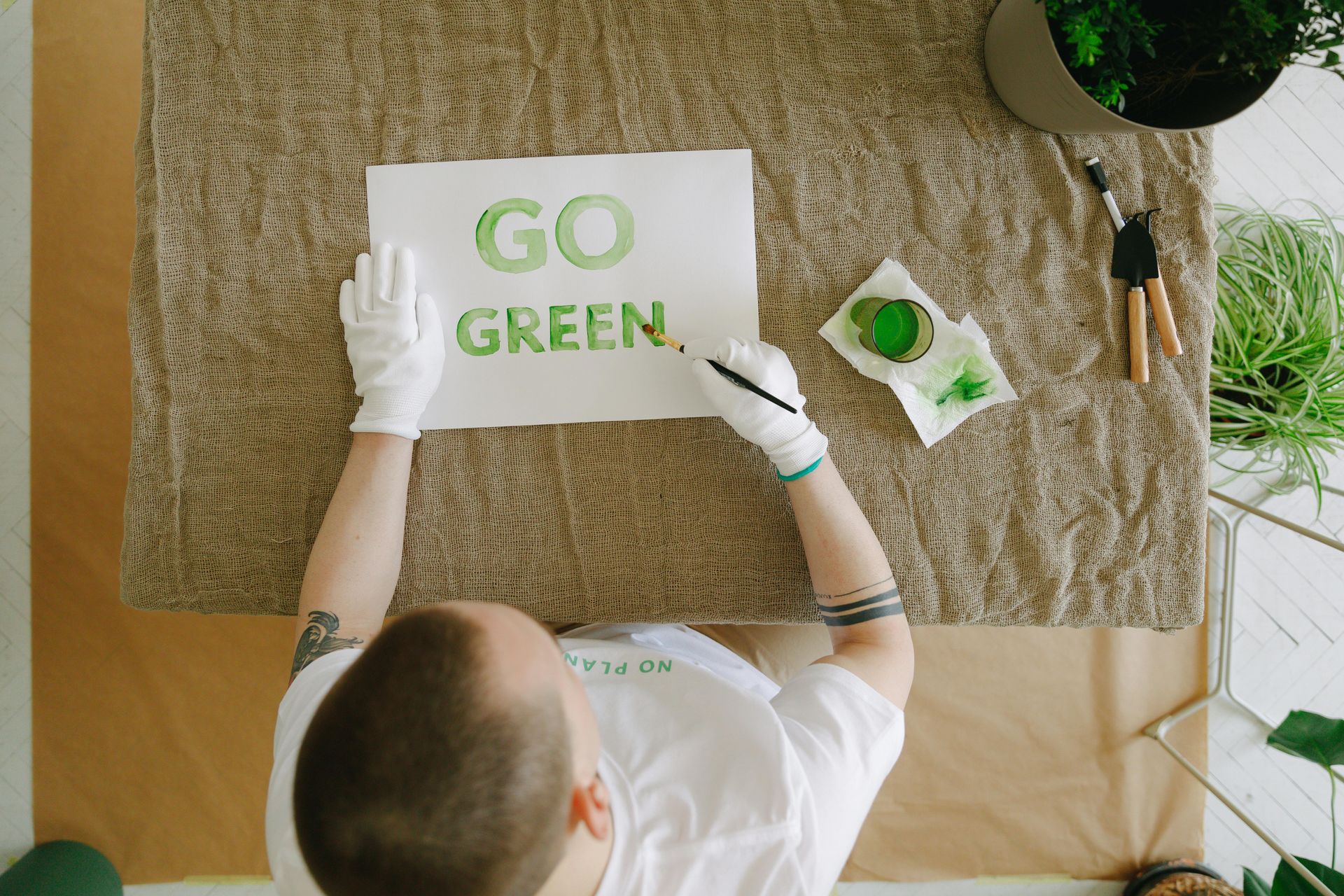 A man is sitting at a table painting a sign that says Go Green