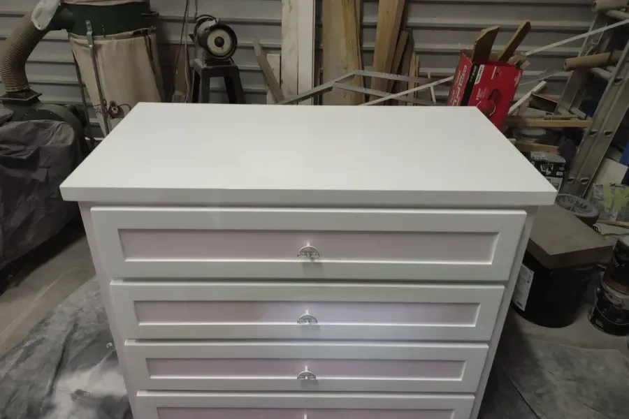 A white dresser with pink drawers is sitting in a garage.
