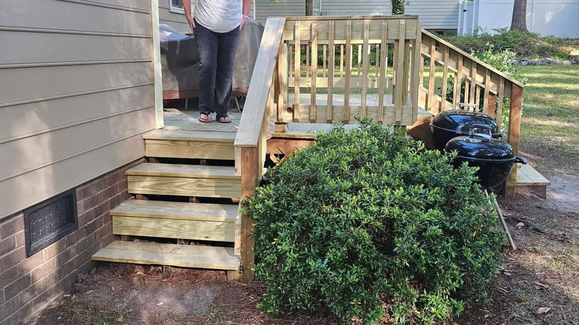Wooden steps and porch with railing beside a house, with a large green shrub in front.
