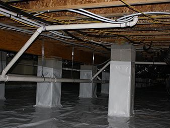 Crawlspace with standing water around wrapped support pillars and exposed pipes under a wooden floor