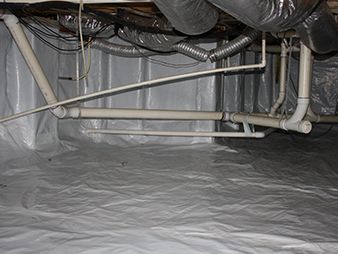 Crawlspace with insulated ducts and exposed white plumbing pipes over a plastic vapor barrier.