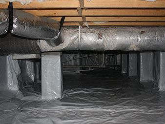 Crawlspace under a house with insulated ducts, floor covering, and wooden joists overhead