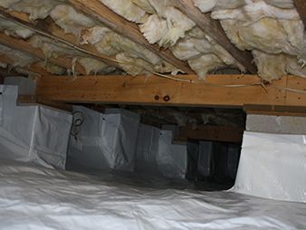 Crawlspace with insulation under floor joists and ductwork wrapped in white plastic coverings