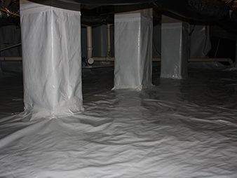 Plastic sheeting covers furniture and floor in a dark room under renovation.