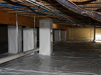 Crawlspace with insulated pipes, wrapped support columns, and plastic vapor barrier on the floor