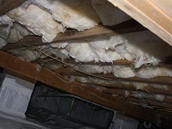 Damaged basement ceiling with exposed insulation, wooden beams, and a hanging black vent or duct