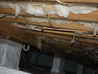 Exposed attic insulation with hanging plastic sheeting and wooden rafters under a roof.