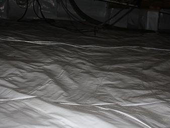 Dim indoor floor covered with a wrinkled white sheet under dark furniture or equipment.