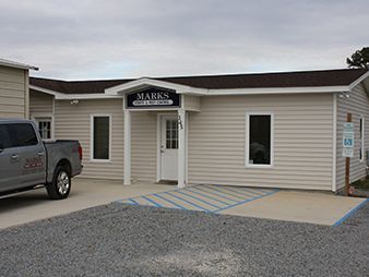 Small beige building with a “MARS” sign, wheelchair ramp markings, and a parked pickup truck outside.