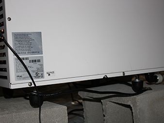 White appliance or machine on cinder blocks with a black cord and label visible near the floor.